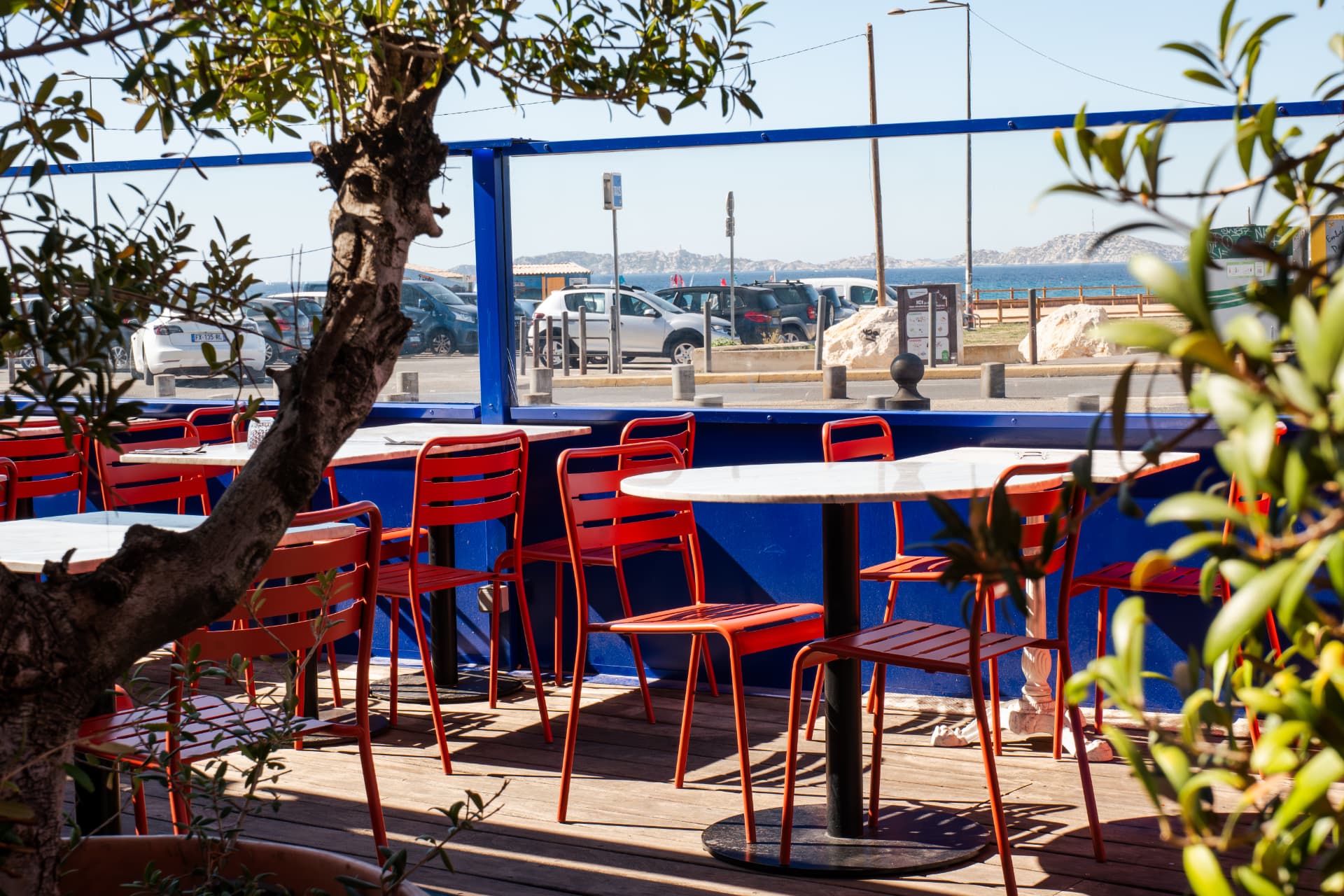 Terrasse du Lou Mar avec tables en marbre, chaises rouges et vue sur la rade