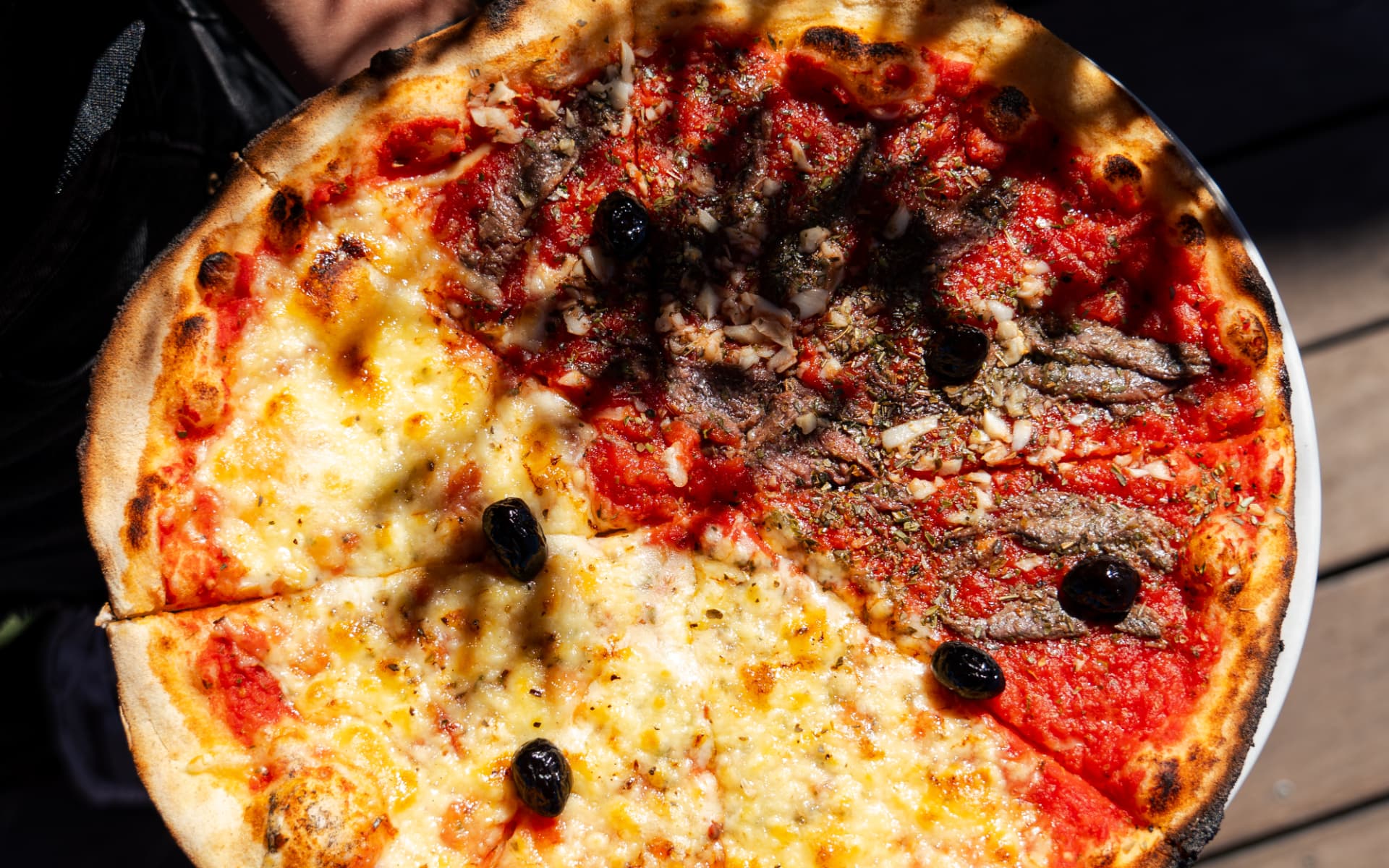 Pizza moitié fromage, moitié anchois et olives, cuite au feu de bois