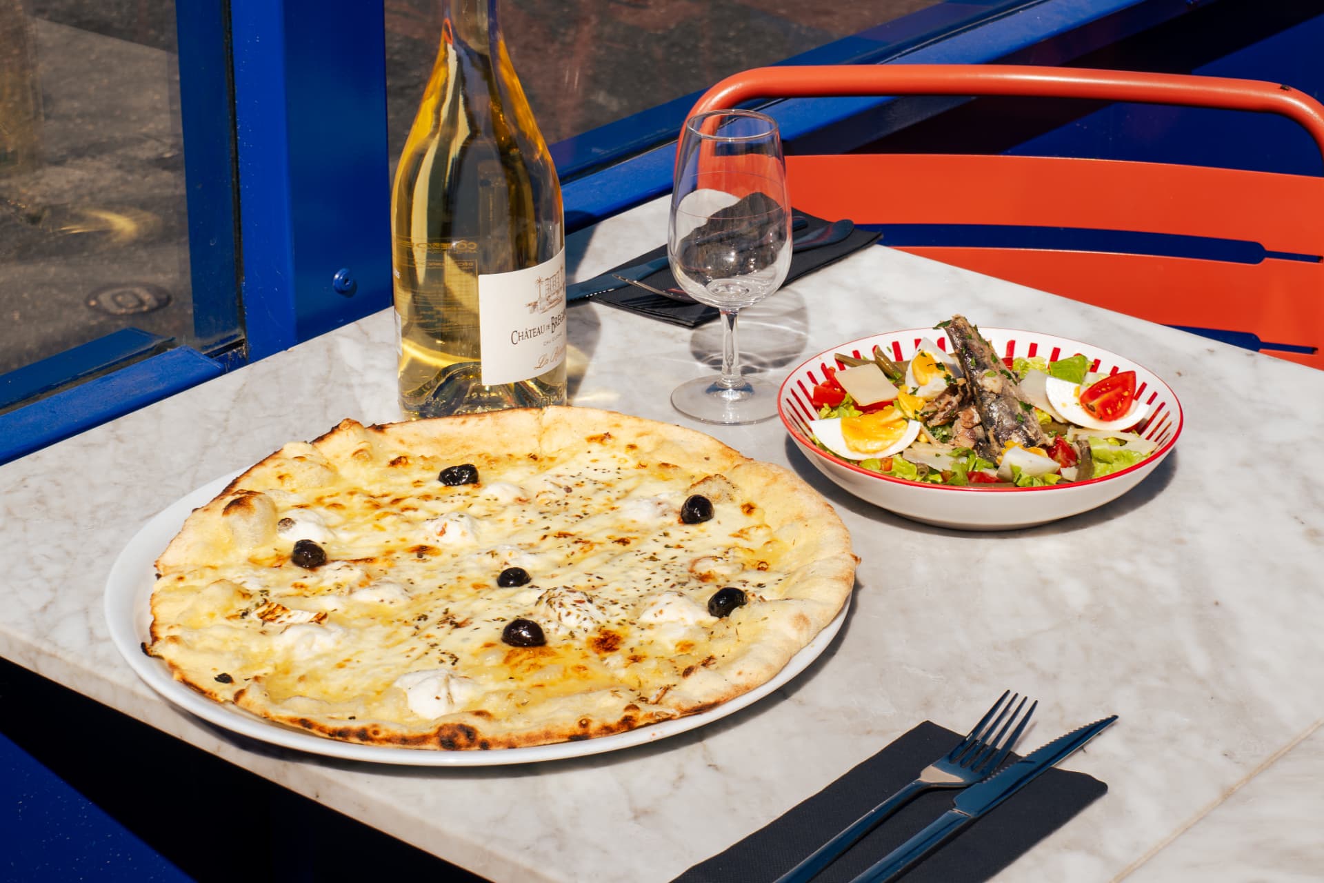 Table en terrasse avec pizza blanche, salade marseillaise et vin blanc